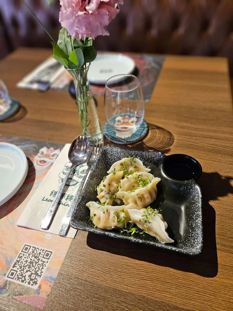 Plato de dim sum contemporáneo emplatado con detalle artístico sobre cerámica blanca, en un ambiente minimalista con acentos en rojo imperial.
